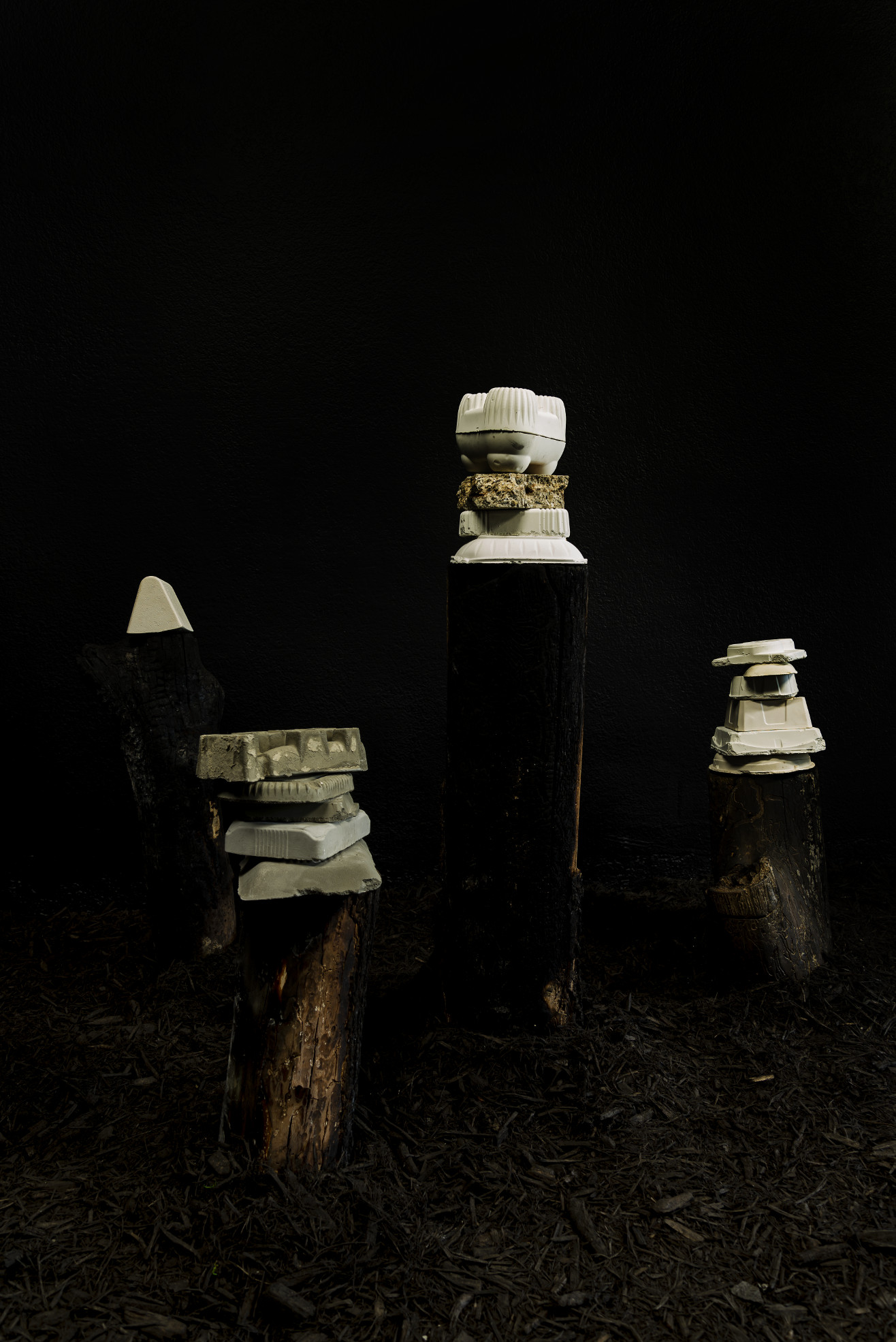 installation view: graffiti'd stumps in all black room with cast plastic objects on them