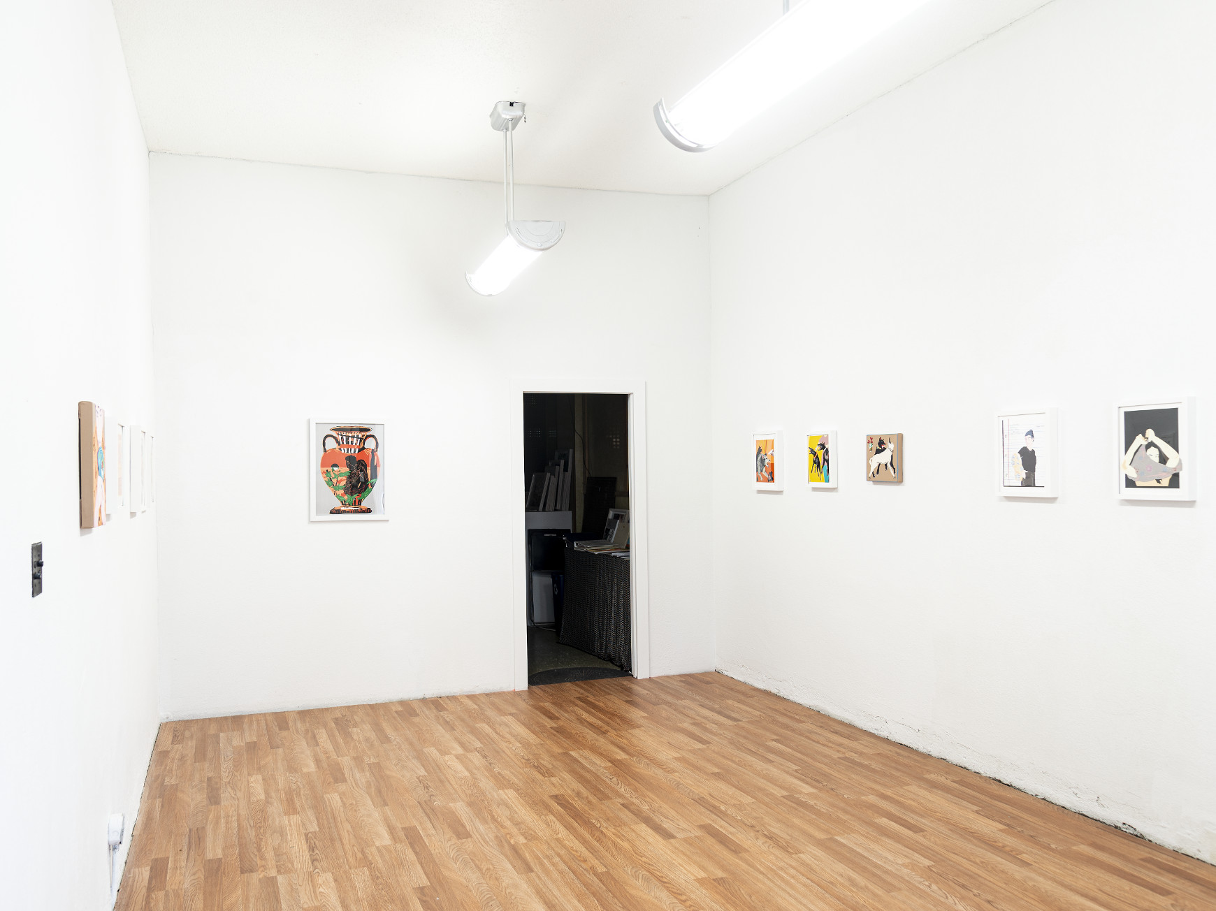 Indoor installation with white walls and wooden floor, small framed collages on the wall